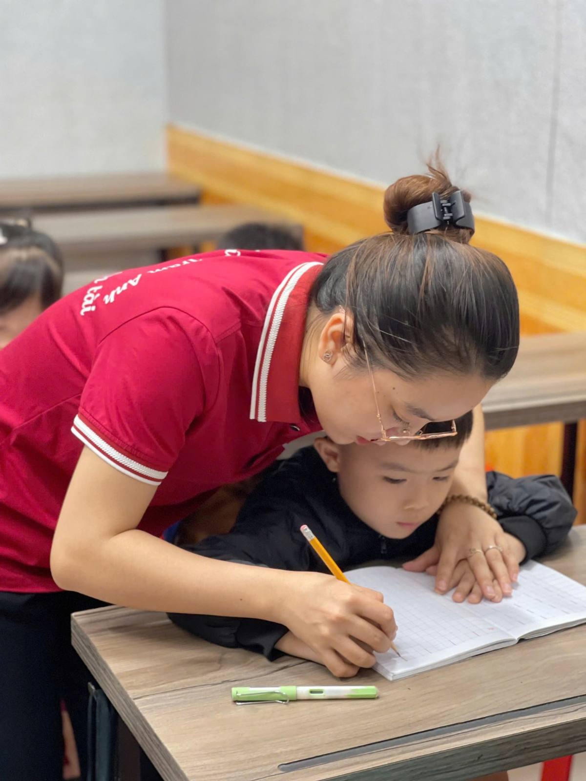 Cô giáo cầm tay bé trai luyện viết bút chì